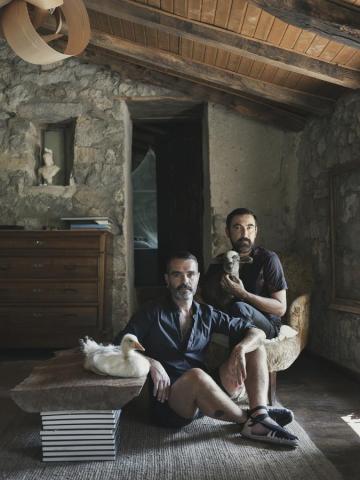 Retrato de Familia de Coque, uno de los fundadores de Santuario Gaia, y Tomás sentados en el suelo y en una butaca, la oca Milo sobre la mesa y la corderita Chloe en brazos.